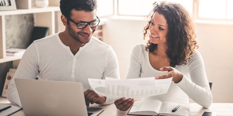 A young man and woman look at their finances and smile happily