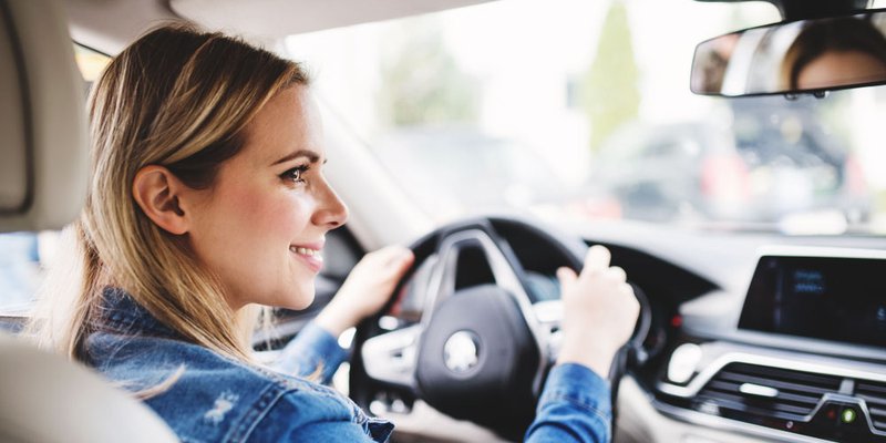 A woman driving her car glances and smiles at her un-pictured passenger