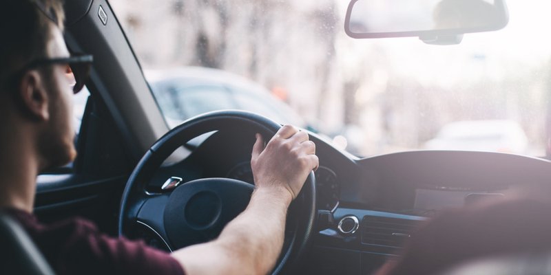 A young man with glasses drives down the street