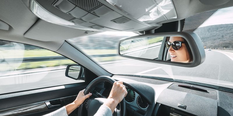 A woman is seen smiling in the rear-view mirror as she drives down a highway
