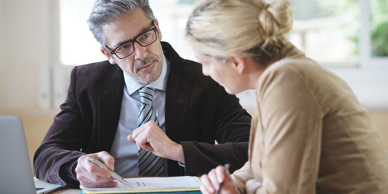 An older man uses his pen to point to a specific section of a document