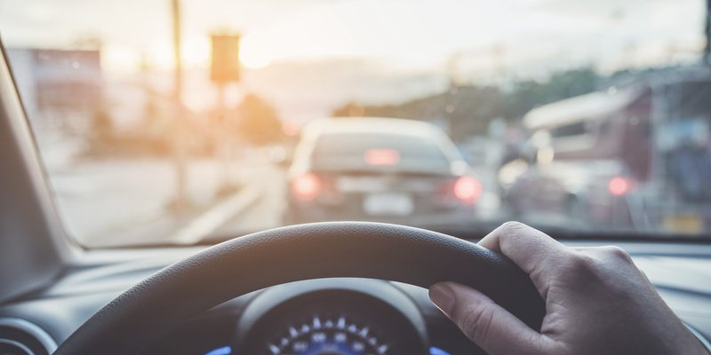 A hand is seen gripping the steering wheel while the car sits in traffic