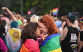 two women embracing at pride in berlin draped in a rainbow flag.jpg